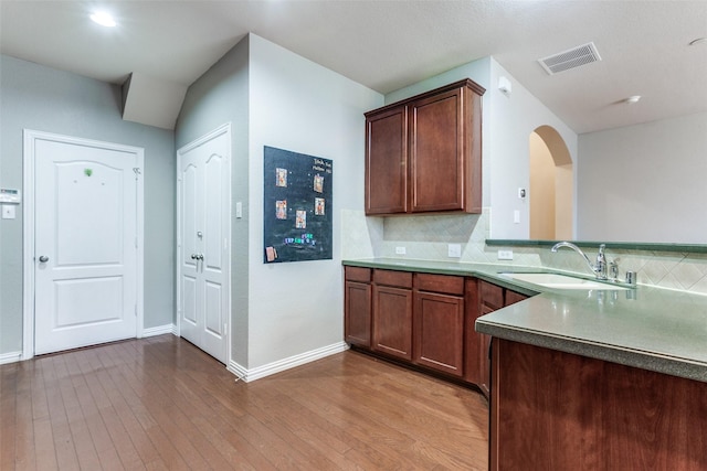 kitchen with arched walkways, wood-type flooring, visible vents, backsplash, and a sink