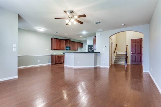 unfurnished living room with arched walkways, dark wood finished floors, stairway, a ceiling fan, and baseboards