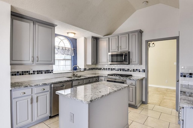 kitchen with light tile patterned floors, gray cabinets, appliances with stainless steel finishes, a sink, and a kitchen island