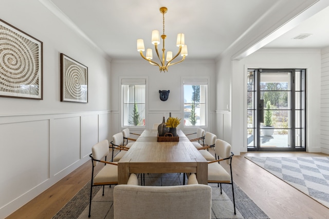 dining area with a decorative wall, wood finished floors, visible vents, ornamental molding, and an inviting chandelier