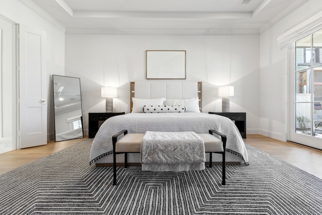 bedroom featuring light wood-type flooring, access to exterior, and a tray ceiling