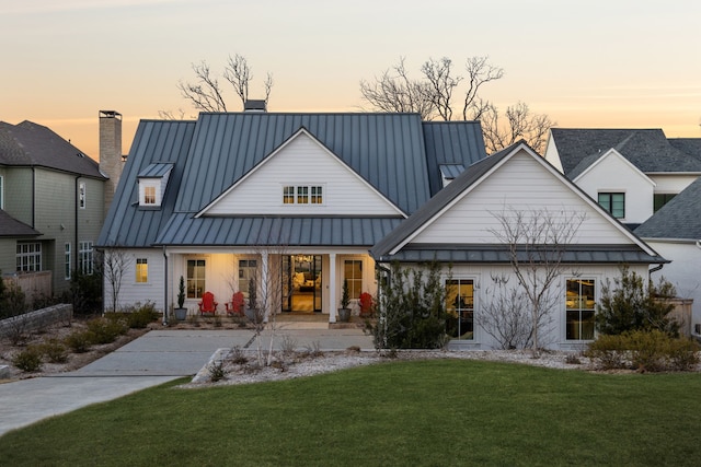 rear view of property with a chimney, a porch, a lawn, a standing seam roof, and metal roof