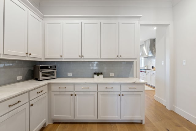 kitchen featuring a toaster, white cabinetry, backsplash, wall chimney exhaust hood, and light wood finished floors