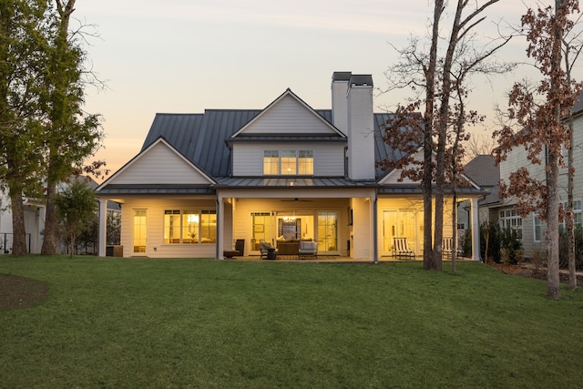 back of house at dusk featuring metal roof, a standing seam roof, a chimney, and a lawn