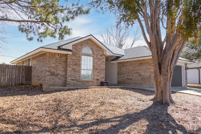 ranch-style house featuring a shingled roof, concrete driveway, an attached garage, fence, and brick siding