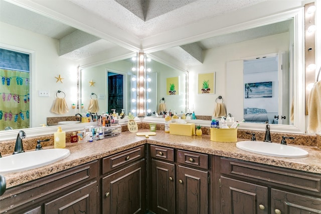 bathroom featuring a textured ceiling, double vanity, ensuite bath, and a sink