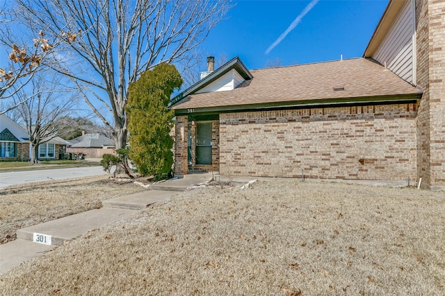 view of front of house with roof with shingles, a chimney, and brick siding