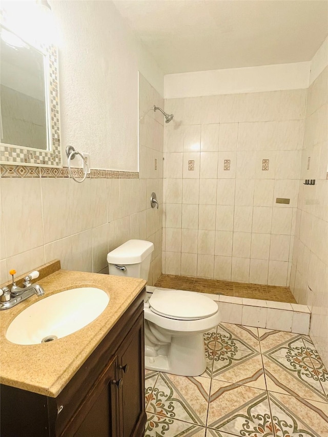 full bath featuring tile walls, toilet, a tile shower, vanity, and tile patterned floors