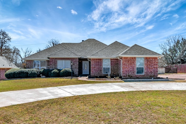 ranch-style home featuring a front lawn, roof with shingles, fence, and brick siding