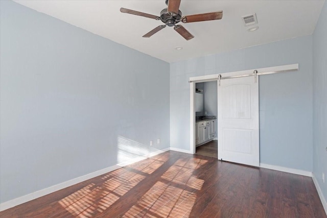 unfurnished bedroom featuring a barn door, visible vents, baseboards, and dark wood finished floors