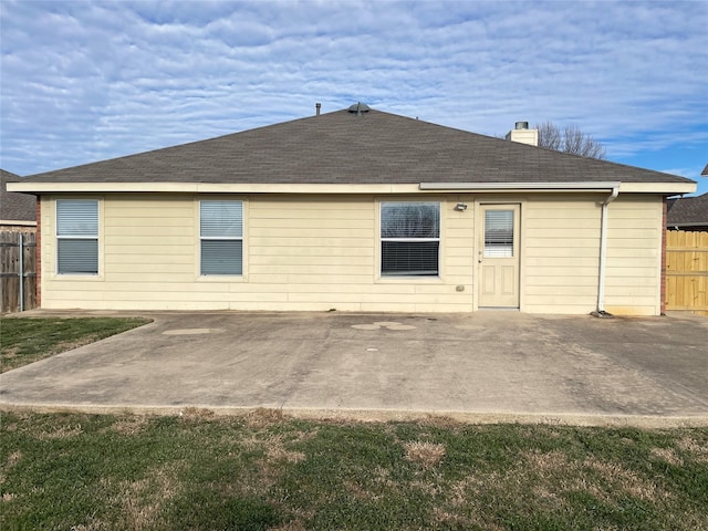 back of property with roof with shingles, a chimney, fence, and a patio