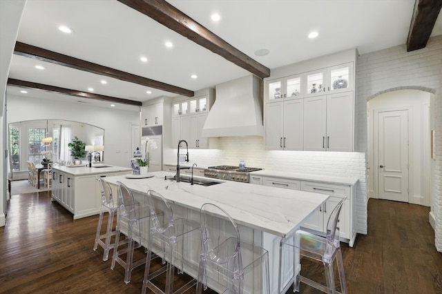 kitchen featuring arched walkways, premium range hood, a spacious island, and a sink