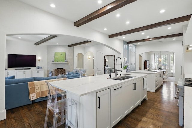 kitchen featuring arched walkways, a spacious island, dark wood-style flooring, white cabinetry, and a sink