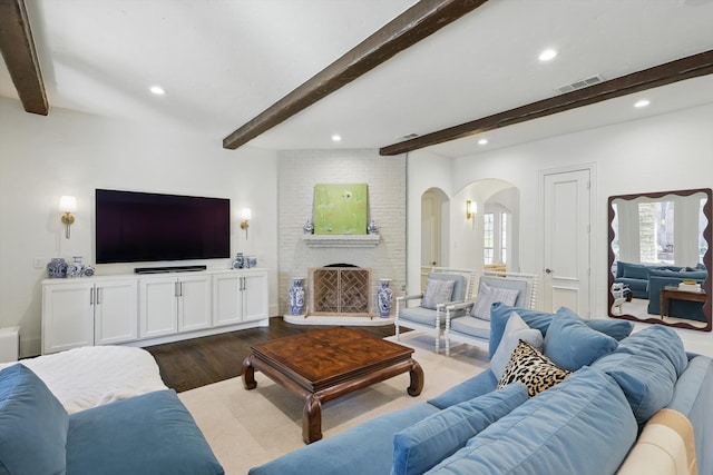 living area featuring dark wood-style floors, beam ceiling, recessed lighting, visible vents, and a brick fireplace