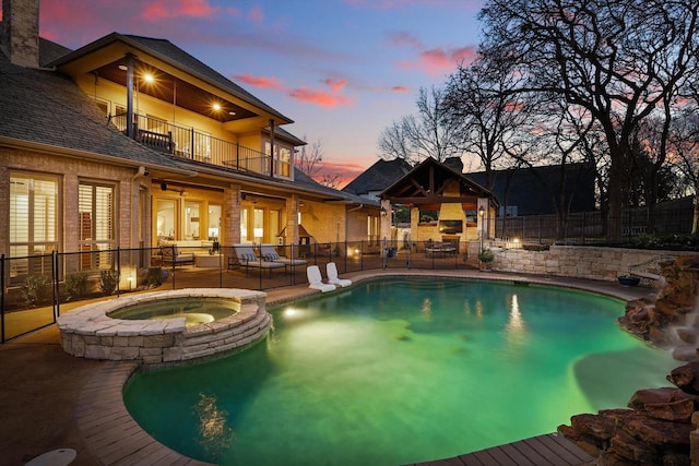 pool at dusk with a pool with connected hot tub, a fireplace, a patio, and fence