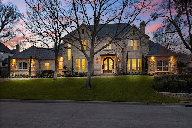 french country style house with stone siding, a lawn, and a chimney