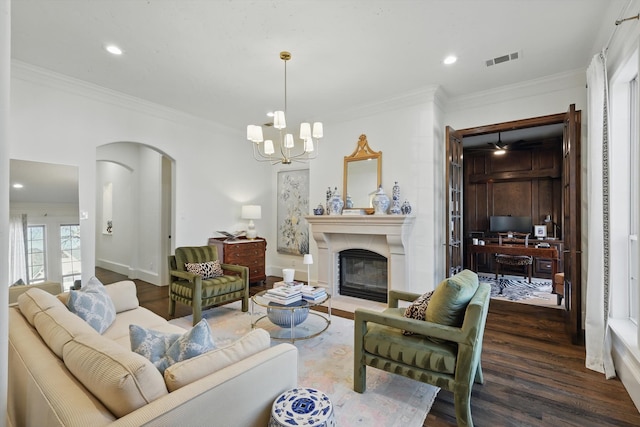 living area featuring arched walkways, visible vents, ornamental molding, a glass covered fireplace, and wood finished floors