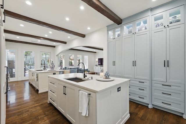 kitchen featuring arched walkways, white cabinets, dark wood-type flooring, a kitchen island with sink, and a sink