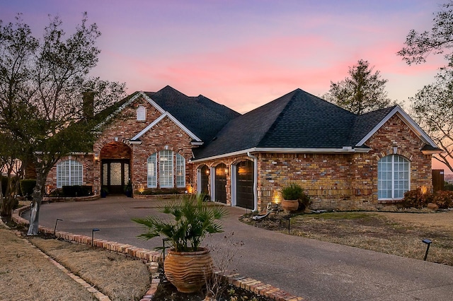 traditional-style home featuring a garage, concrete driveway, brick siding, and a shingled roof