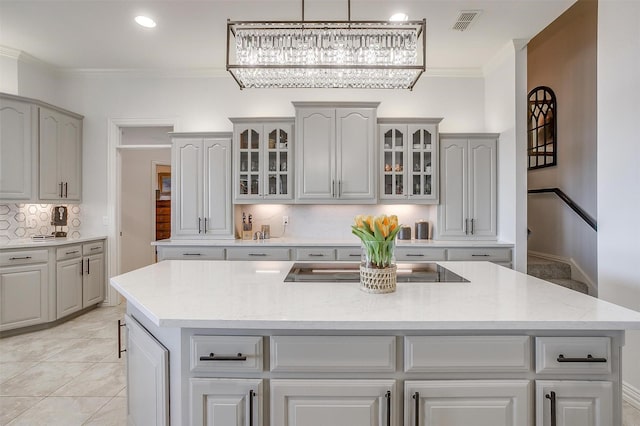 kitchen with a center island, black electric stovetop, visible vents, ornamental molding, and glass insert cabinets