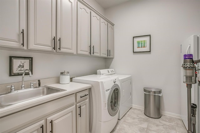 clothes washing area featuring baseboards, a sink, cabinet space, and washer and dryer