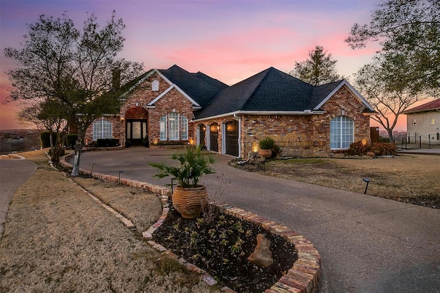 traditional-style home featuring a garage, driveway, brick siding, and a shingled roof