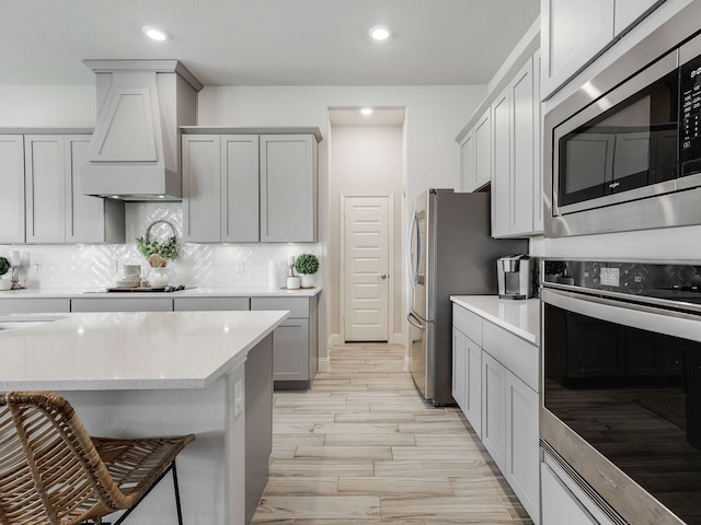 kitchen featuring tasteful backsplash, light stone countertops, custom exhaust hood, stainless steel appliances, and recessed lighting