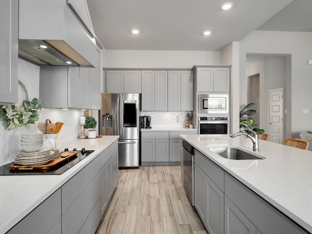 kitchen with gray cabinets, decorative backsplash, appliances with stainless steel finishes, a sink, and premium range hood