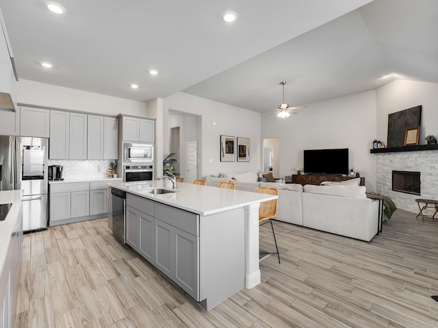 kitchen with appliances with stainless steel finishes, gray cabinets, light countertops, a stone fireplace, and a sink