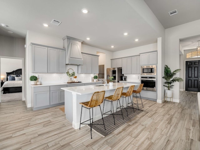 kitchen featuring gray cabinets, light countertops, custom range hood, visible vents, and appliances with stainless steel finishes