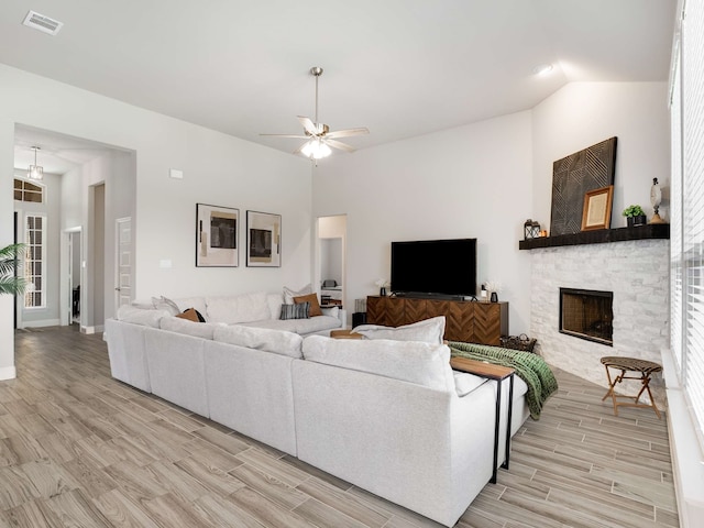 living area with light wood finished floors, visible vents, lofted ceiling, ceiling fan, and a stone fireplace