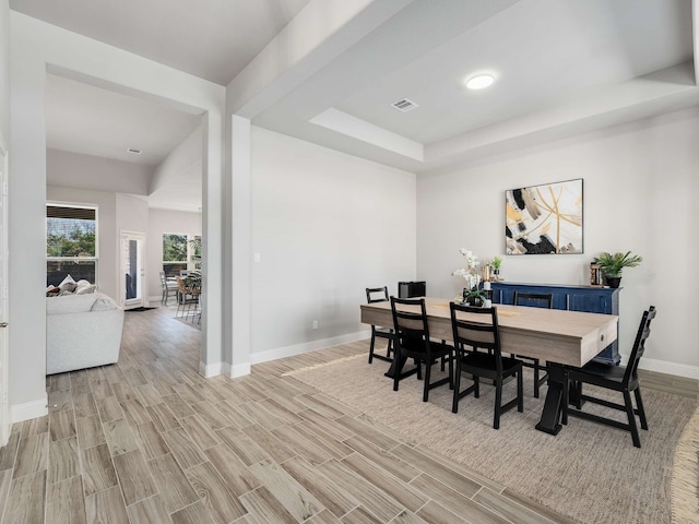 dining space featuring wood finish floors, a raised ceiling, visible vents, and baseboards