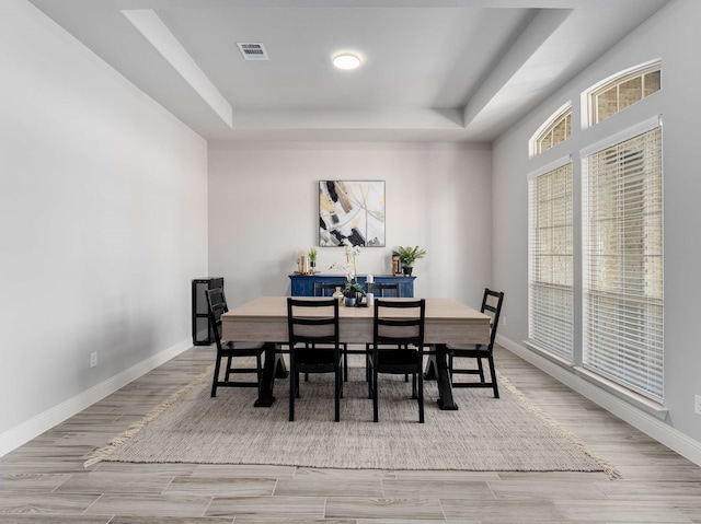 dining space with light wood-type flooring, a raised ceiling, visible vents, and baseboards