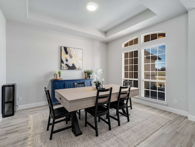 dining area with light wood-style floors, a raised ceiling, and baseboards