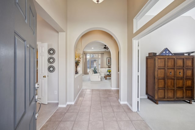 entryway with light tile patterned floors, baseboards, arched walkways, a ceiling fan, and a high ceiling