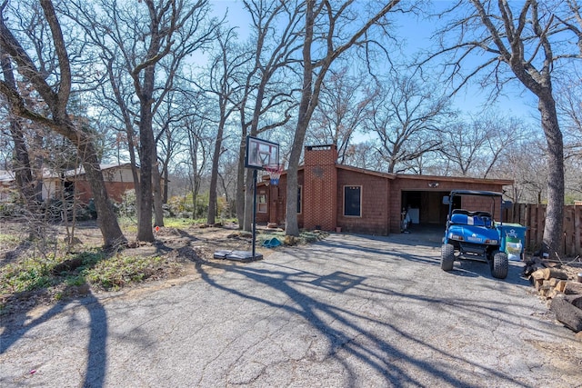 view of side of home with driveway, a chimney, an attached garage, and fence