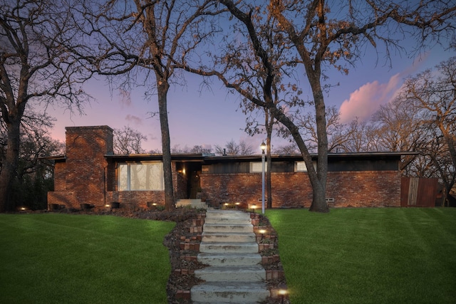 mid-century inspired home with a chimney, a lawn, and brick siding