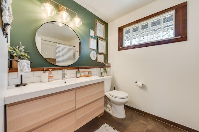 bathroom featuring tile patterned flooring, toilet, vanity, baseboards, and tasteful backsplash