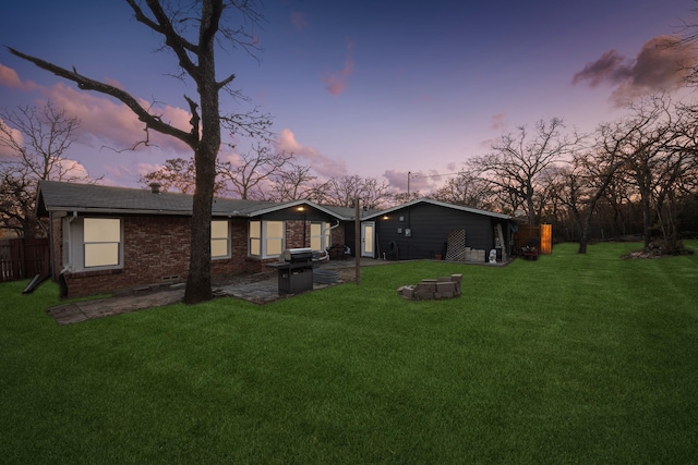 back of property at dusk featuring brick siding, a yard, fence, and a patio