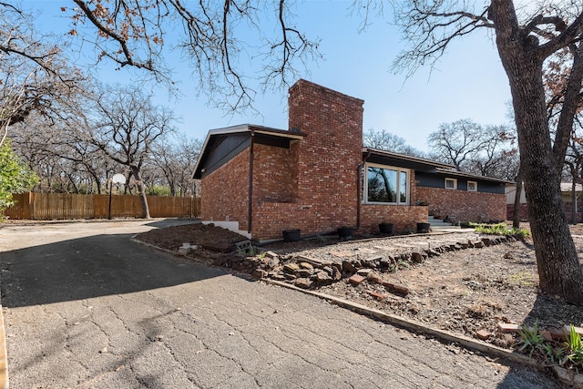 view of home's exterior featuring driveway, brick siding, fence, and a chimney