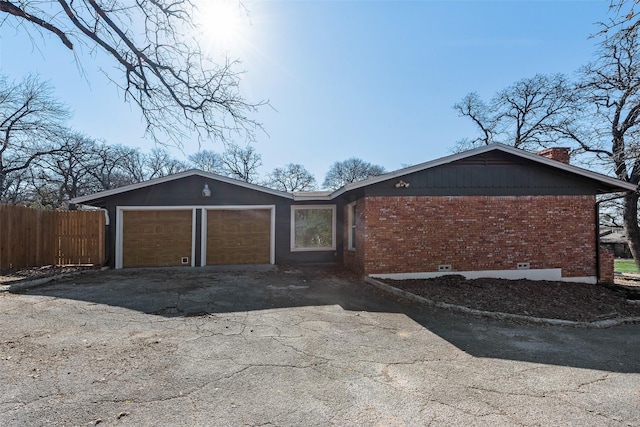 single story home featuring brick siding, a chimney, fence, a garage, and driveway