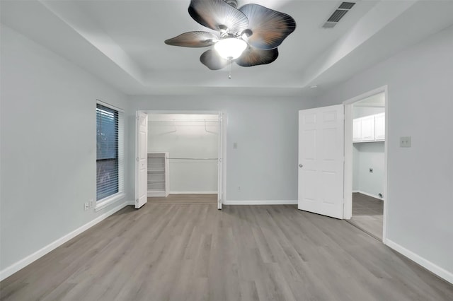 unfurnished bedroom with baseboards, visible vents, a raised ceiling, and light wood-style flooring