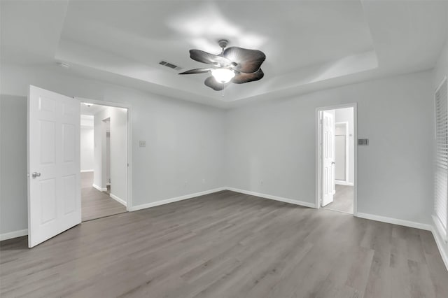 spare room featuring baseboards, visible vents, a raised ceiling, and wood finished floors