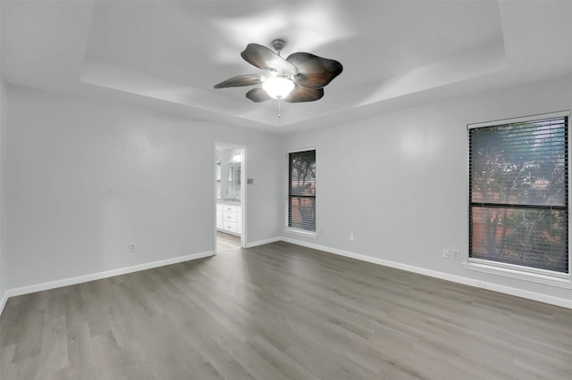 unfurnished room featuring ceiling fan, wood finished floors, a raised ceiling, and baseboards