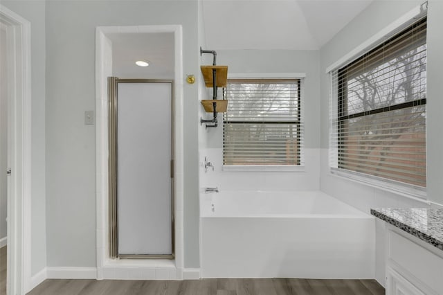 bathroom featuring wood finished floors, vanity, baseboards, a bath, and a stall shower