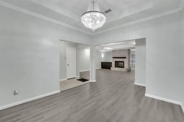 unfurnished living room with a raised ceiling, visible vents, a brick fireplace, wood finished floors, and baseboards