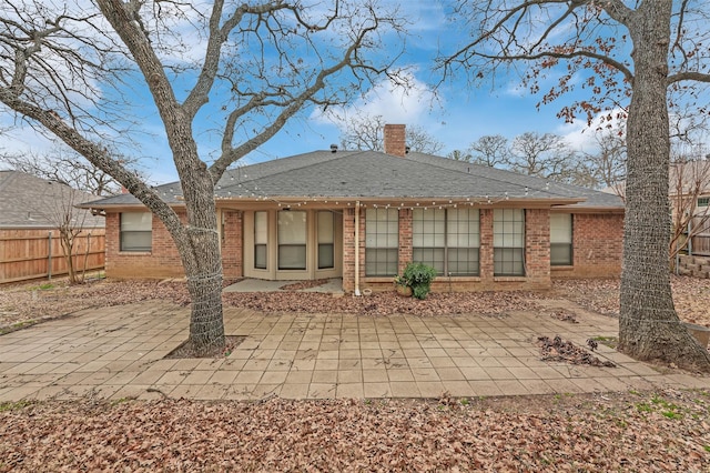 rear view of house featuring a patio, brick siding, a chimney, and fence