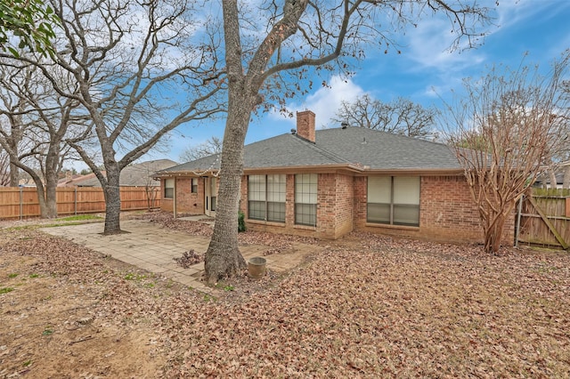 back of house featuring a patio, a fenced backyard, brick siding, a shingled roof, and a chimney