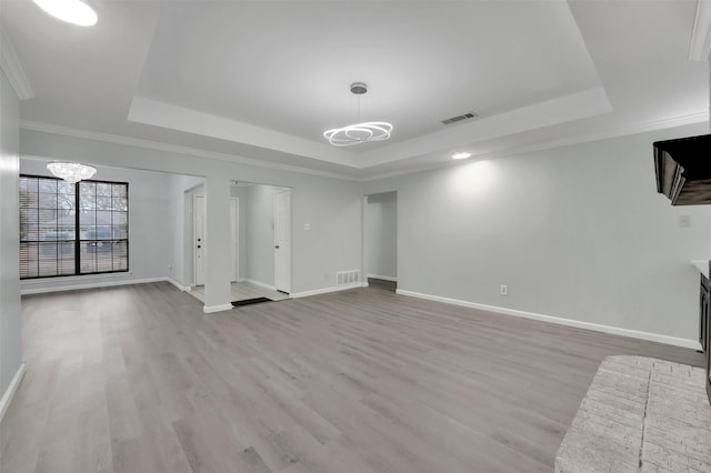 unfurnished living room with an inviting chandelier, visible vents, a tray ceiling, and light wood-style flooring