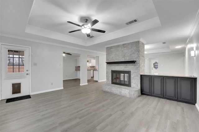 unfurnished living room with a fireplace, visible vents, ornamental molding, light wood finished floors, and a raised ceiling